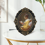 An oval-shaped black picture frame with embossed flourish details. It is designed for both wall and tabletop display.