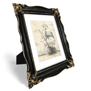 An ornate black picture frame with gold accents, displaying a mountain range artwork.