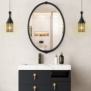 An oval-shaped mirror with a traditional frame in a bathroom setting, reflecting a modern shower stall and bathroom decor.