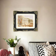 A vintage picture frame includes artwork on a wall above a bed with decorative pillows and a vase of flowers.