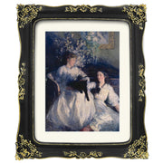 Framed artwork of two women with a black cat, surrounded by flowers, in a decorative gold and black frame.