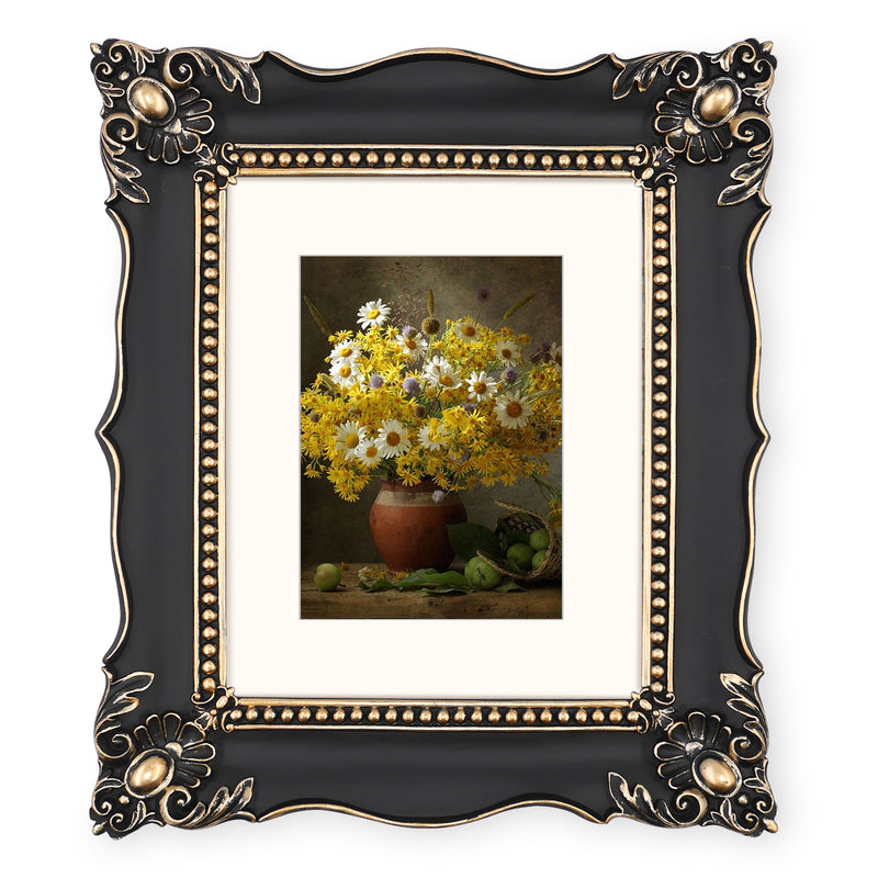 An ornate black picture frame with gold accents, displaying a floral artwork.