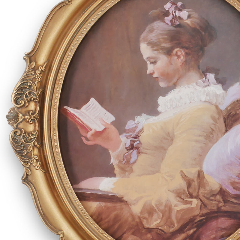 An oval-shaped, gold-colored picture frame with embossed details, containing a framed artwork of a person reading.
