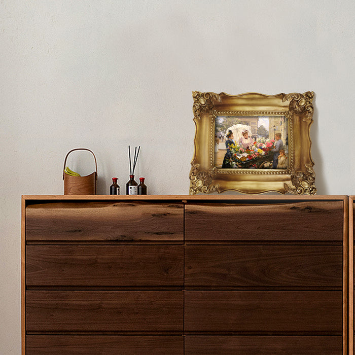 Wooden dresser with decorative items including a framed painting on a plain wall.