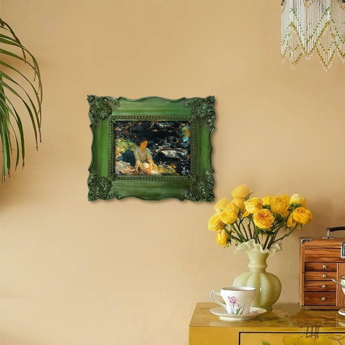 Decorative green frame with a painting on a beige wall, next to a vase of yellow flowers and a cabinet.