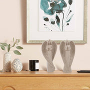 Decorative items including angel statues, a candle, and vases on a wooden surface with a floral painting in the background.