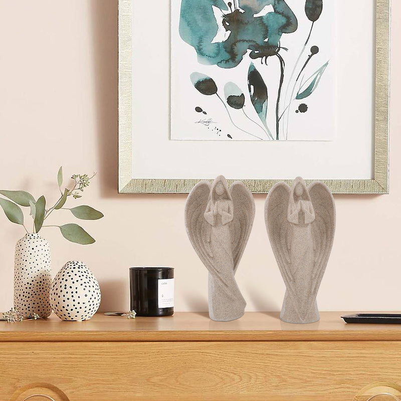 Decorative items including angel statues, a candle, and vases on a wooden surface with a floral painting in the background.