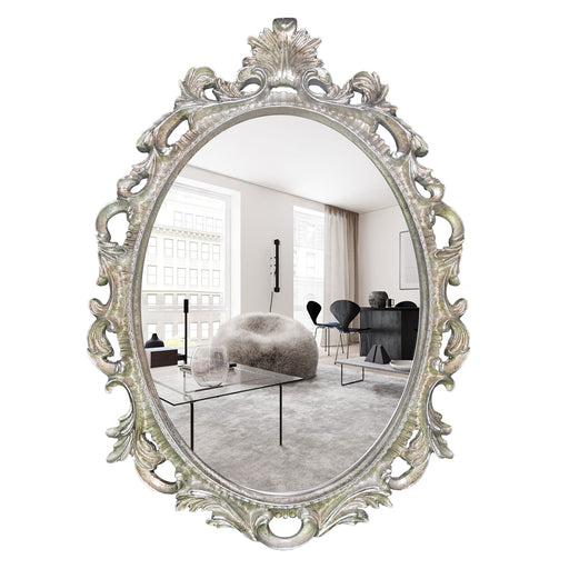 An oval mirror with a scroll design in an antique silver finish, reflecting a well-lit interior room.