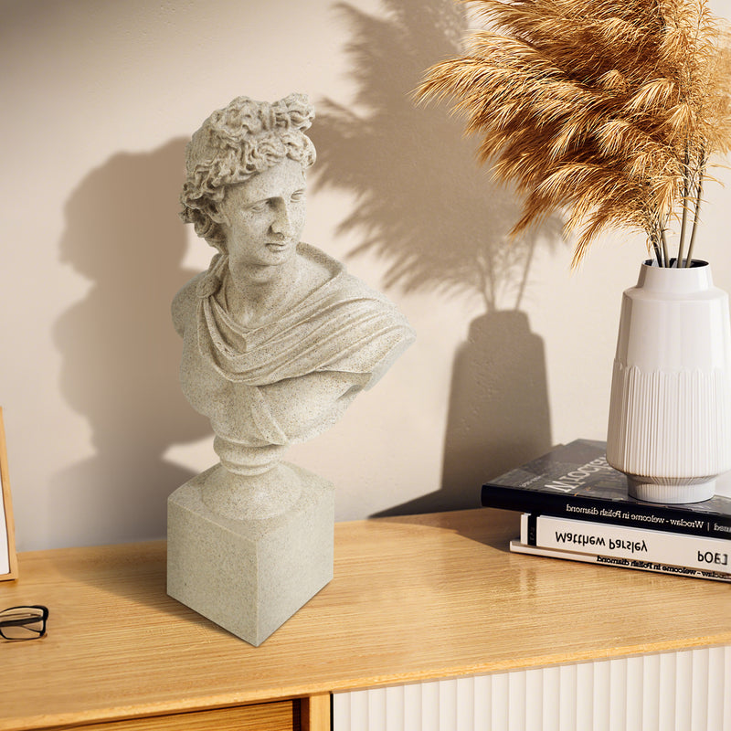 Statue bust on a wooden surface with books and a vase in the background.