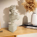 Statue bust on a wooden surface with books and a vase in the background.