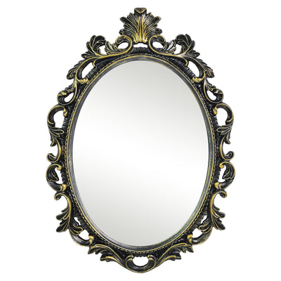 An oval mirror with a scroll design in an antique black with gold finish, reflecting a well-lit interior room.