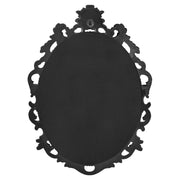 An oval mirror with a scroll design in an antique black with gold finish, reflecting a well-lit interior room.