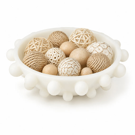 An off-white ceramic bowl with a scalloped edge, filled with decorative natural-fiber balls and wooden spheres on a white background.