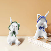 Two resin figurines of sitting rabbits with hats, one with eyes covered and one with a mouth covered, in different poses.