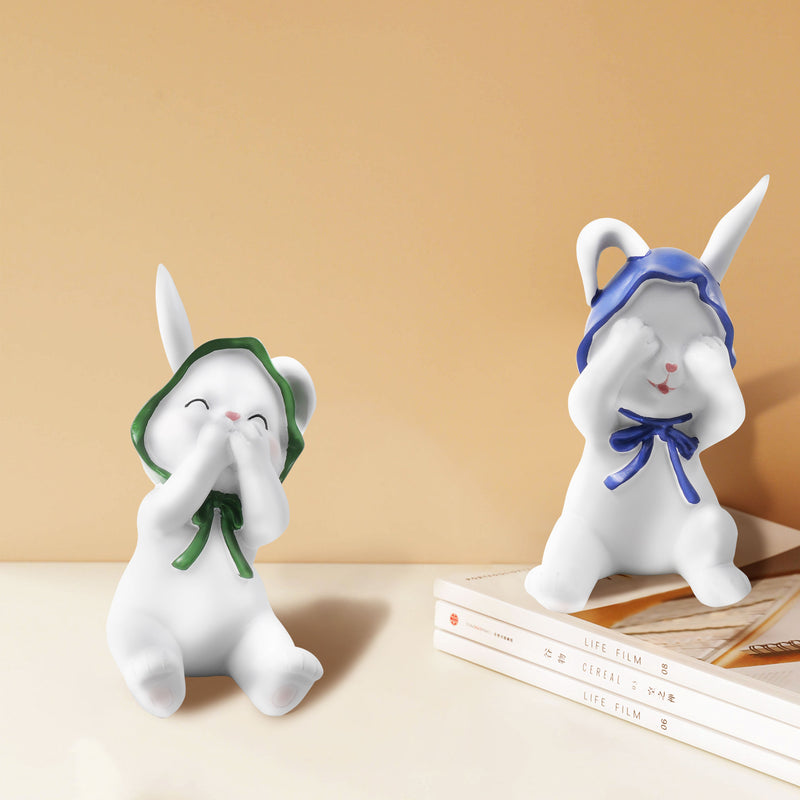 Two resin figurines of sitting rabbits with hats, one with eyes covered and one with a mouth covered, in different poses.