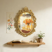 Decorative gold-framed mirror on a wall with a shelf below containing an open book, small plant, and decorative items.