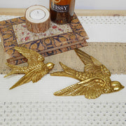Two gold bird figurines on a textured surface with a bottle and candle in the background.