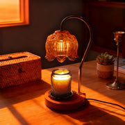 Decorative candle warmer lamp with a warm glow on a wooden surface, surrounded by a wicker box and a small plant.