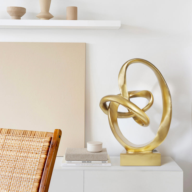 Gold abstract sculpture on a white surface with a neutral background