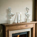 Two classical busts on a wooden mantelpiece with books in front of a fireplace.
