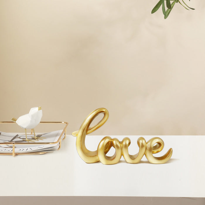 A gold-colored sculpture in the form of the word 'LOVE' in a cursive script, designed for tabletop decor.