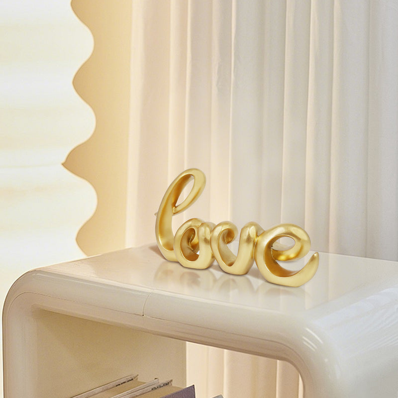 A gold-colored sculpture in the form of the word 'LOVE' in a cursive script, designed for tabletop decor.