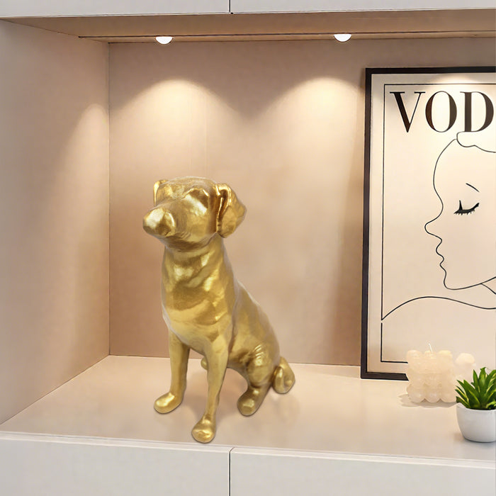Gold dog statue on a shelf with a framed picture and a plant in the background.