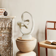 Abstract sculpture on a wooden pedestal in a room with a chair and decorative items.