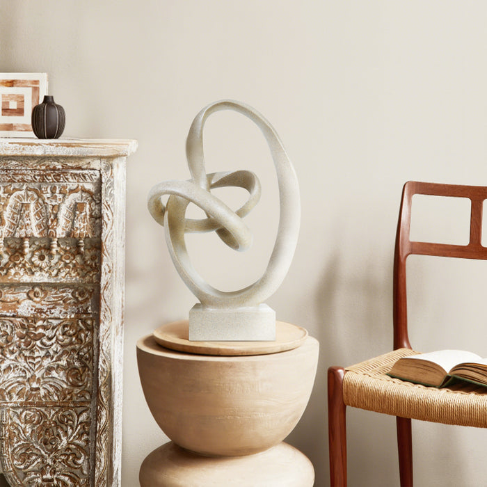 Abstract sculpture on a wooden pedestal in a room with a chair and decorative items.