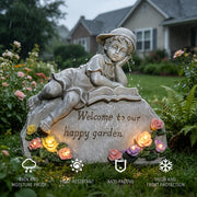 Decorative garden statue with a child reading a book, surrounded by flowers and text 'Welcome to our happy garden'.