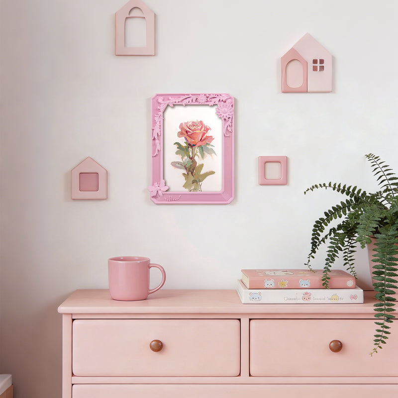 Pink dresser with a mug, books, and a framed picture of a rose on a light pink wall.
