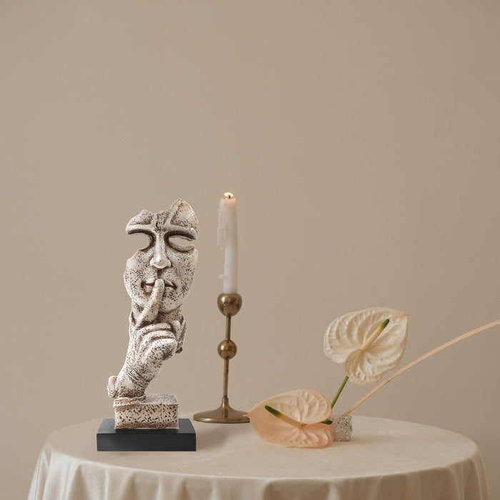 A sculpture of a human figure with an index finger to their lips, indicating silence or quiet. The figure appears to be made of a textured, possibly stone or concrete-like material, and is placed on a dark base.