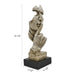A sculpture of a human figure with an index finger to their lips, indicating silence or quiet. The figure appears to be made of a textured, possibly stone or concrete-like material, and is placed on a dark base.