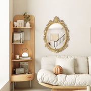 An oval mirror with a scroll design in an antique gold finish, reflecting a well-lit interior room.