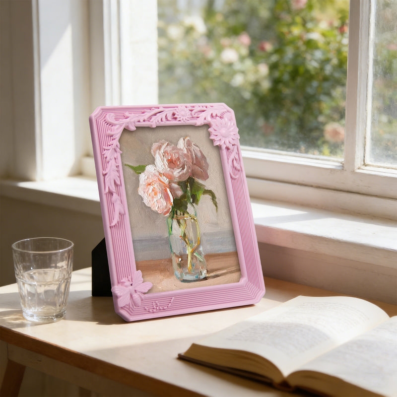 Pink decorative frame with a floral photo on a table by a window