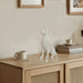 White dog sculpture on a wooden cabinet with books and mugs in a room.