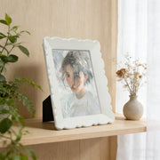 White decorative photo frame with a portrait on a wooden surface next to a plant and vase.