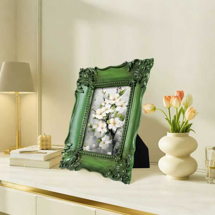 Decorative green frame with floral artwork on a table with a lamp and a vase in the background.