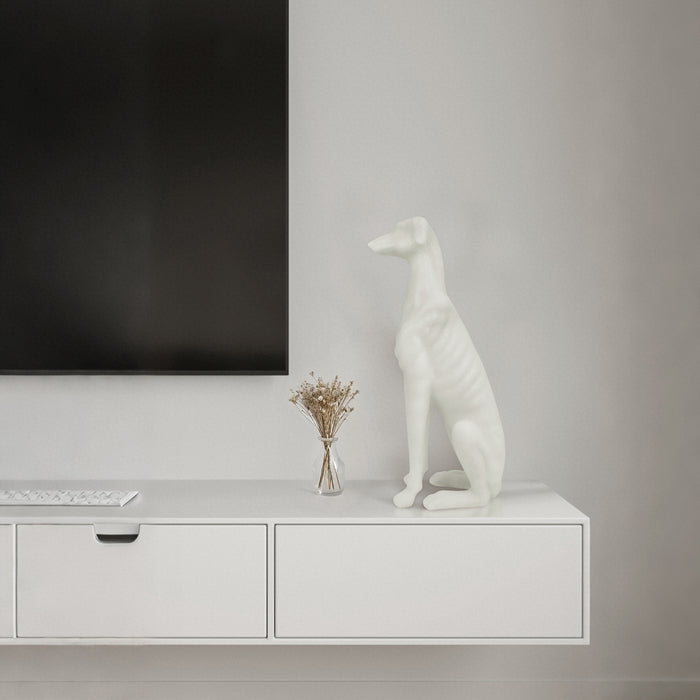White dog sculpture on a white console table with a television in the background.