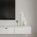 White dog sculpture on a white console table with a television in the background.