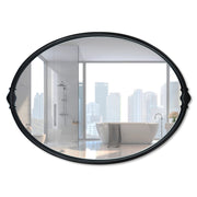 An oval-shaped mirror with a traditional frame in a bathroom setting, reflecting a modern shower stall and bathroom decor.