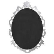 An oval mirror with a scroll design in an antique silver finish, reflecting a well-lit interior room.