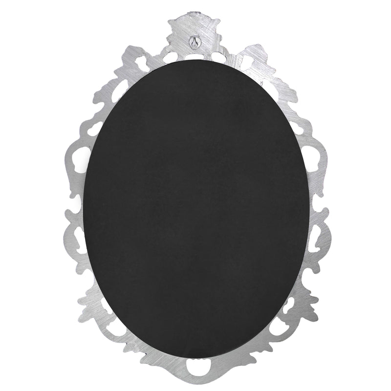 An oval mirror with a scroll design in an antique silver finish, reflecting a well-lit interior room.