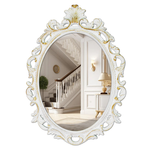 An oval mirror with a scroll design in an white with gold finish, reflecting a well-lit interior room.