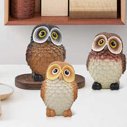 A set of three resin owl figurines, painted in different colors, is displayed side by side.