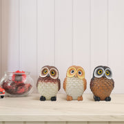 A set of three resin owl figurines, painted in different colors, is displayed side by side.