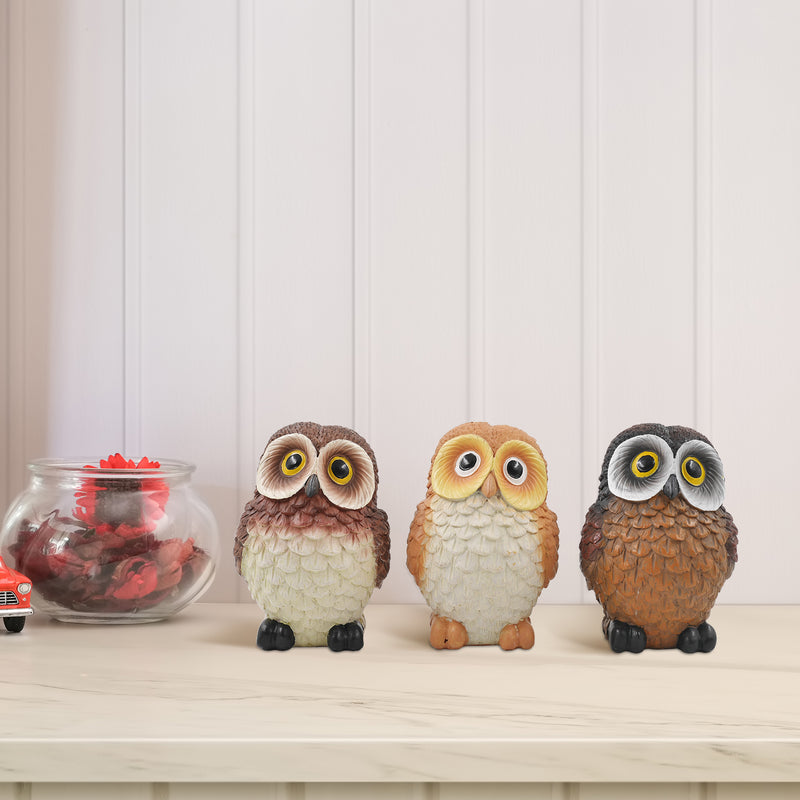 A set of three resin owl figurines, painted in different colors, is displayed side by side.