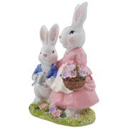 A hand-painted resin figurine of a rabbit family, comprising a mother and child, dressed in decorative outfits and holding a floral basket and a metal pot.